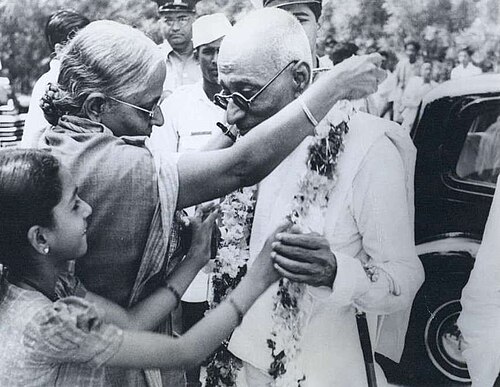An elderly woman blessing C. Rajagopalachari in a crowd as a young girl looks on.